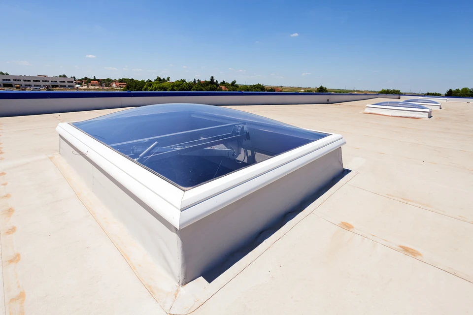 Toit terrasse d'un bâtiment commercial avec lanterneau vitré rectangulaire installé sur membrane d'étanchéité blanche