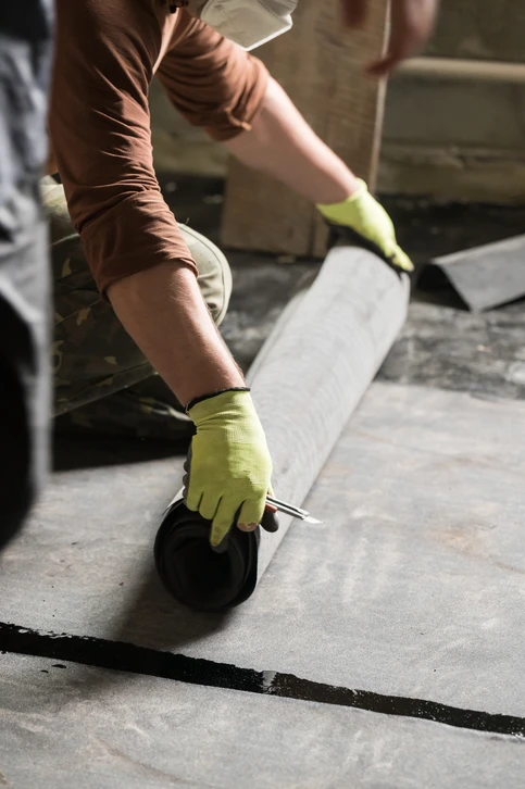 Ouvrier en chantier appliquant un produit d'étanchéité noir sur dalle béton extérieure