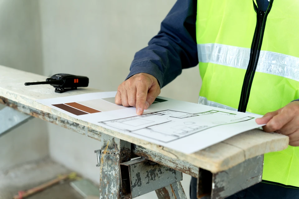 Vue aérienne ou en légère plongée d'une toiture terrasse rénovée montrant l'ensemble du processus fini : membrane d'étanchéité en EPDM ou PVC gris anthracite fraîchement posée, joints de soudure visibles, relevés d'étanchéité périmétriques sur acrotères en briques, un lanterneau dôme translucide en polycarbonate monté sur costière, sortie de ventilation, et bâtiment résidentiel en briques en arrière-plan. La photo doit transmettre la qualité professionnelle, la complétude des travaux (charpente/structure visible en fond, platelage/structure OSB, isolation, étanchéité et éléments techniques) et la fiabilité d'une intervention intégrée.